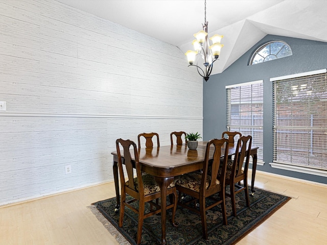 dining room with lofted ceiling, wood walls, light wood-type flooring, and a notable chandelier