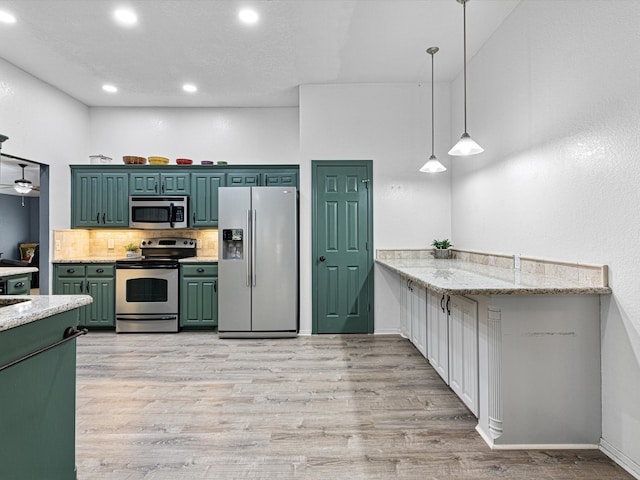 kitchen with appliances with stainless steel finishes, light stone countertops, light wood-type flooring, and pendant lighting