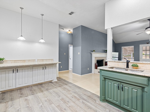 kitchen featuring light wood-type flooring, vaulted ceiling, decorative light fixtures, light stone counters, and green cabinetry