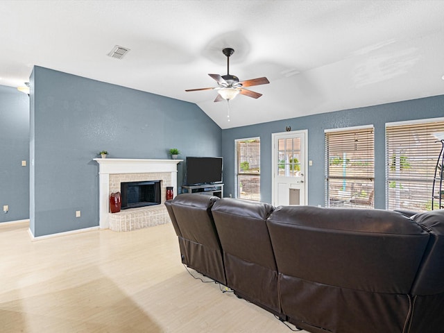 living room featuring light wood-style flooring, a fireplace, visible vents, baseboards, and vaulted ceiling