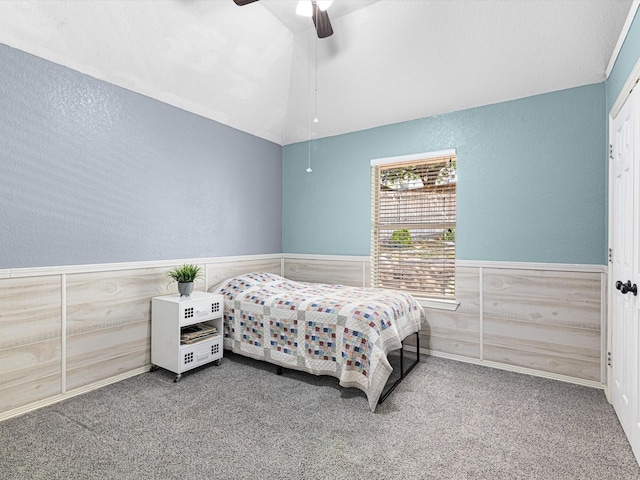 bedroom featuring a textured wall, carpet, wainscoting, and vaulted ceiling