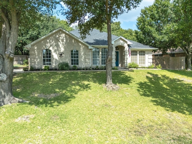 ranch-style house featuring a front lawn, roof with shingles, and fence