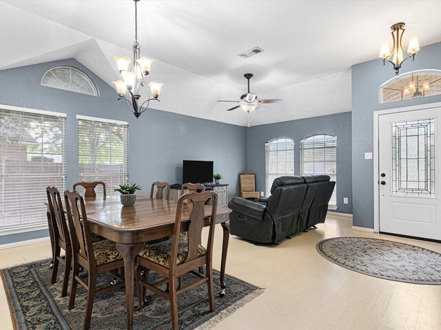 dining space with vaulted ceiling, light hardwood / wood-style flooring, ceiling fan with notable chandelier, and plenty of natural light