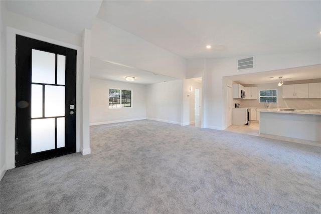 unfurnished living room with light carpet, lofted ceiling, visible vents, and baseboards