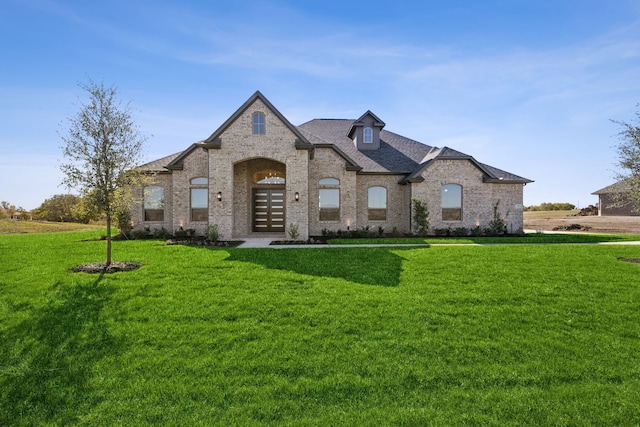 french country home with brick siding, a front yard, and a shingled roof