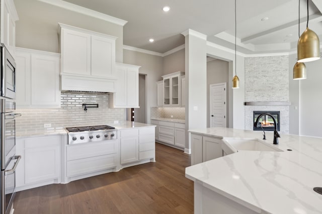 kitchen with stainless steel appliances, dark wood-type flooring, white cabinets, a sink, and a stone fireplace