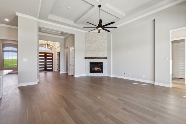 unfurnished living room with coffered ceiling, ceiling fan with notable chandelier, crown molding, wood-type flooring, and a stone fireplace