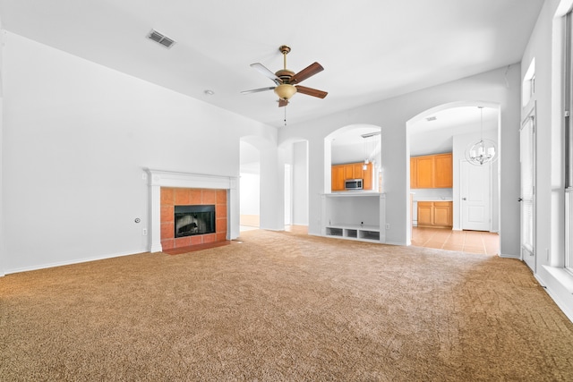 unfurnished living room featuring light colored carpet, ceiling fan with notable chandelier, and a tile fireplace