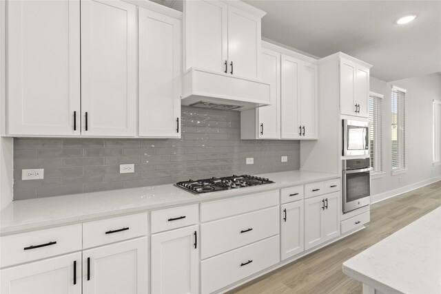 kitchen with custom exhaust hood, appliances with stainless steel finishes, light hardwood / wood-style flooring, and white cabinets