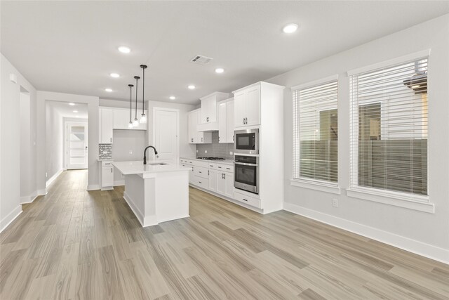 kitchen with appliances with stainless steel finishes, sink, an island with sink, pendant lighting, and light hardwood / wood-style flooring