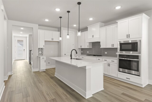 kitchen with hanging light fixtures, a center island with sink, sink, white cabinets, and appliances with stainless steel finishes