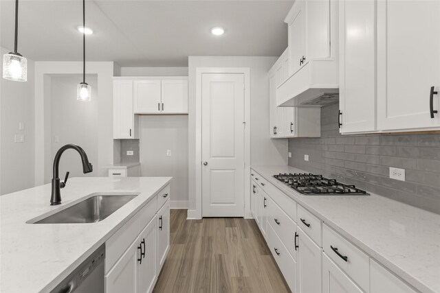 kitchen with hanging light fixtures, white cabinetry, stainless steel appliances, sink, and light stone counters