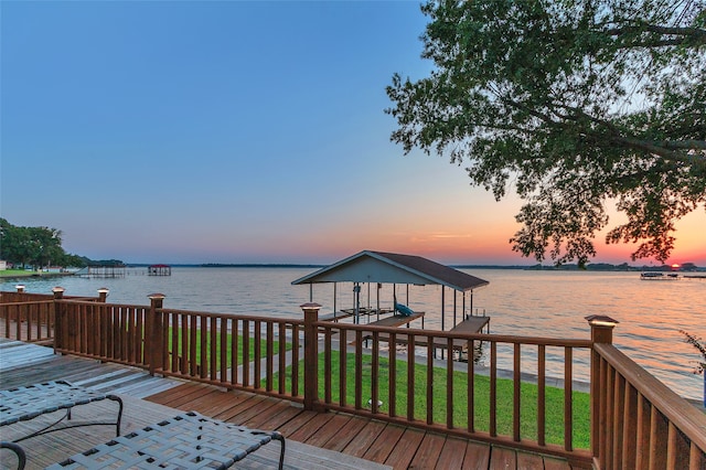 deck at dusk with a dock, a lawn, and a water view