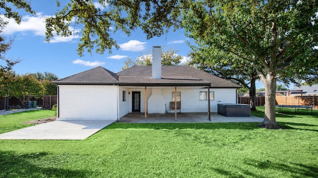 back of house with a hot tub, a lawn, a trampoline, and a patio