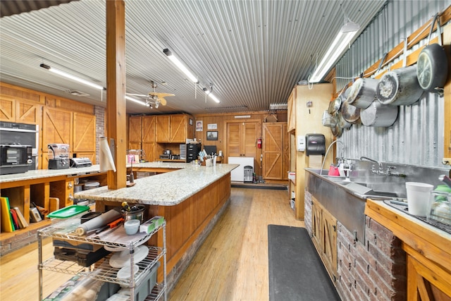 kitchen with ceiling fan, light wood-type flooring, wood walls, and light stone countertops