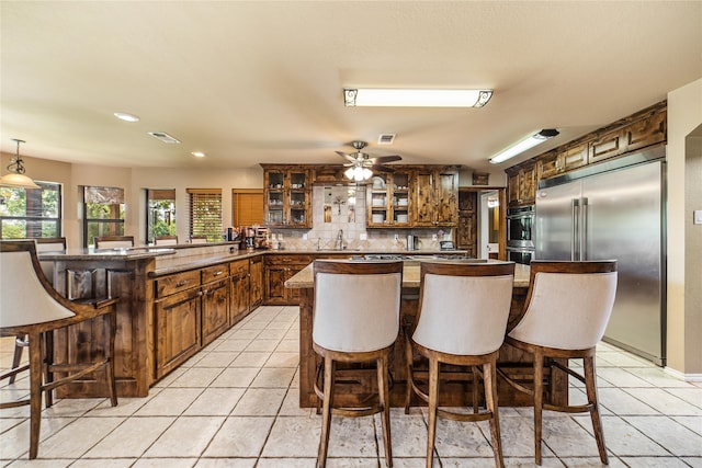 kitchen with light tile patterned flooring, kitchen peninsula, backsplash, and stainless steel built in fridge