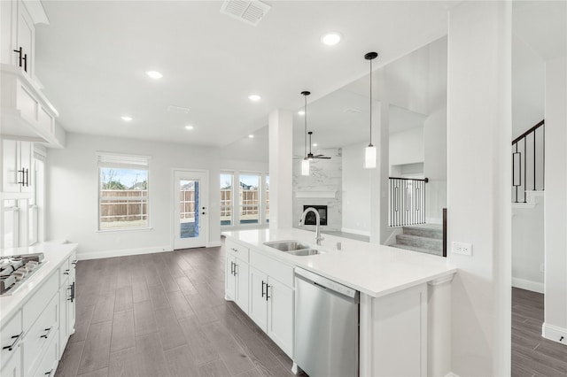 kitchen with sink, a large fireplace, decorative light fixtures, stainless steel appliances, and white cabinets