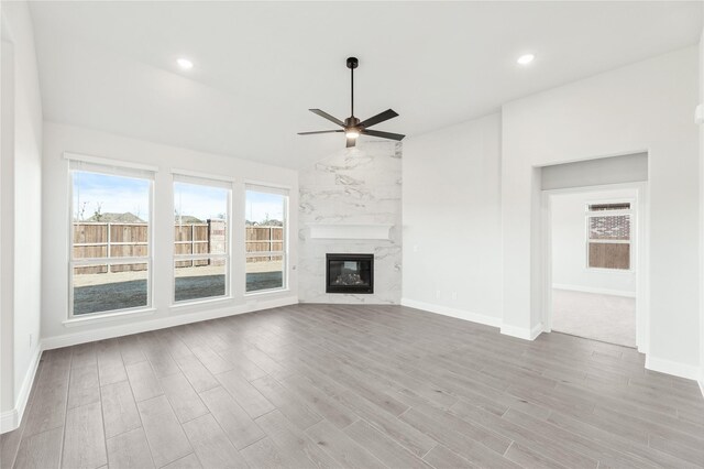 unfurnished living room with light hardwood / wood-style floors, vaulted ceiling, a high end fireplace, and ceiling fan