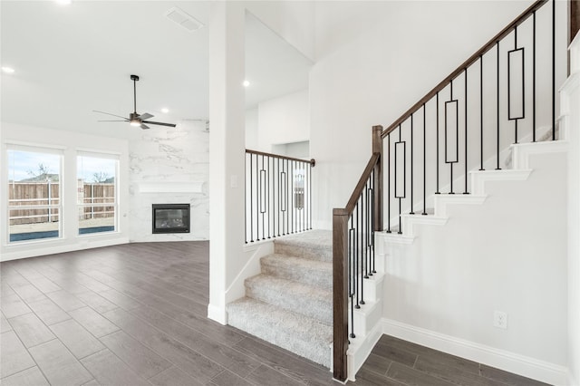 staircase featuring ceiling fan, wood-type flooring, and a fireplace