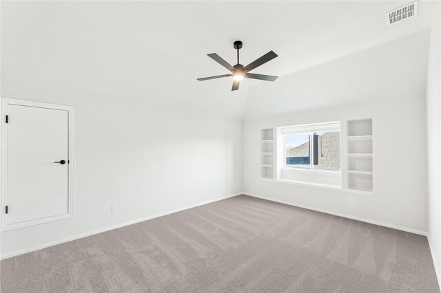 carpeted empty room featuring ceiling fan, vaulted ceiling, and built in features