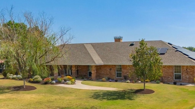 view of front facade featuring a shingled roof, brick siding, a front yard, and solar panels