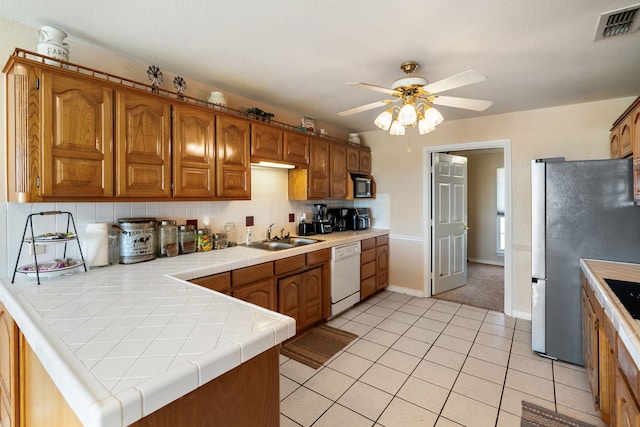 kitchen featuring tile counters, stainless steel refrigerator, backsplash, white dishwasher, and sink