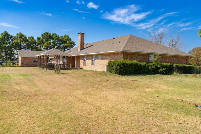 rear view of house featuring fence, a lawn, a chimney, and brick siding