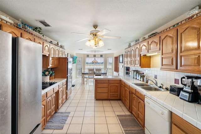 kitchen with a textured ceiling, dishwasher, tile counters, stainless steel refrigerator, and sink