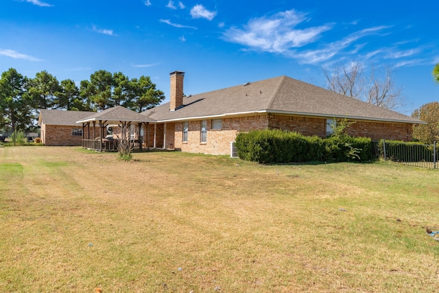 rear view of house featuring fence, a lawn, a chimney, and brick siding