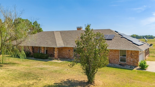 view of front of property with brick siding, an attached garage, a shingled roof, roof mounted solar panels, and a front yard