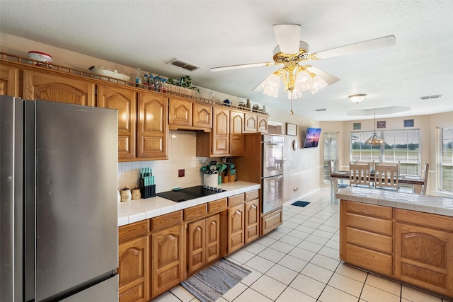 kitchen featuring tasteful backsplash, tile counters, ceiling fan, stainless steel appliances, and visible vents