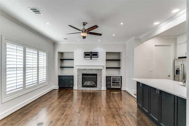 unfurnished living room with crown molding, dark hardwood / wood-style floors, a tile fireplace, and built in features