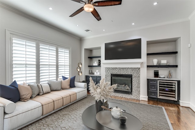 living room featuring hardwood / wood-style flooring, ornamental molding, built in features, beverage cooler, and a fireplace