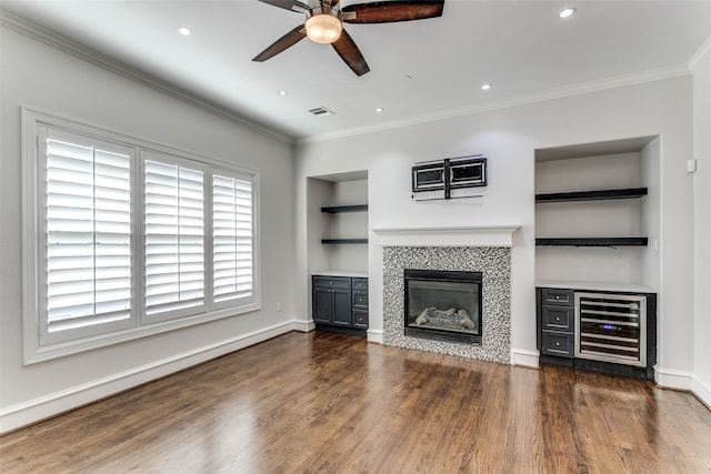 unfurnished living room featuring a tile fireplace, wine cooler, crown molding, dark hardwood / wood-style flooring, and ceiling fan