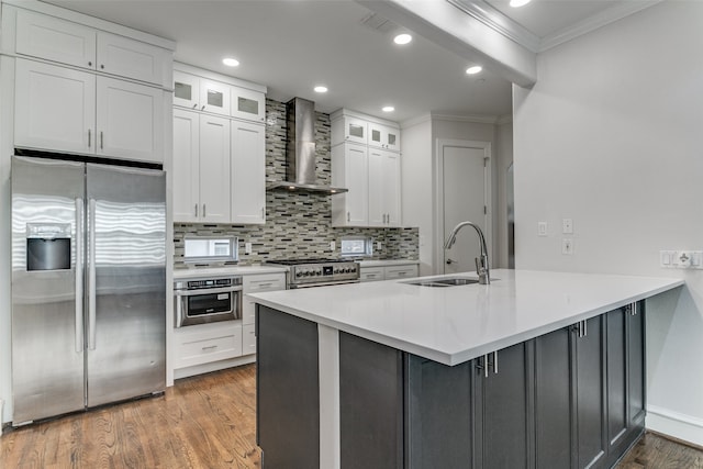 kitchen with appliances with stainless steel finishes, sink, wood-type flooring, white cabinetry, and wall chimney exhaust hood