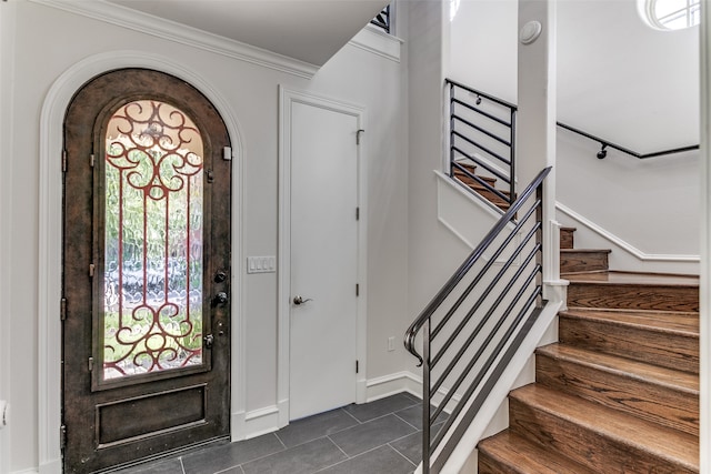 foyer entrance with dark tile patterned floors and crown molding