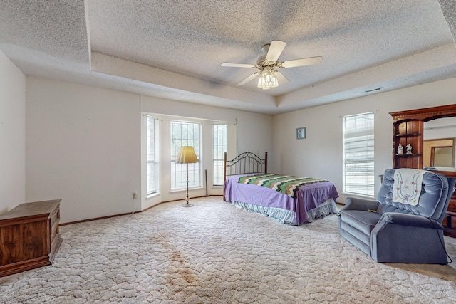 bedroom featuring a textured ceiling, a tray ceiling, multiple windows, and light colored carpet