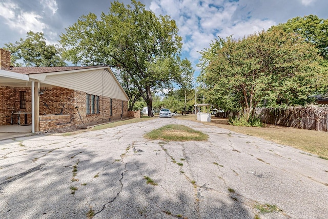 exterior space with driveway, brick siding, a chimney, and fence