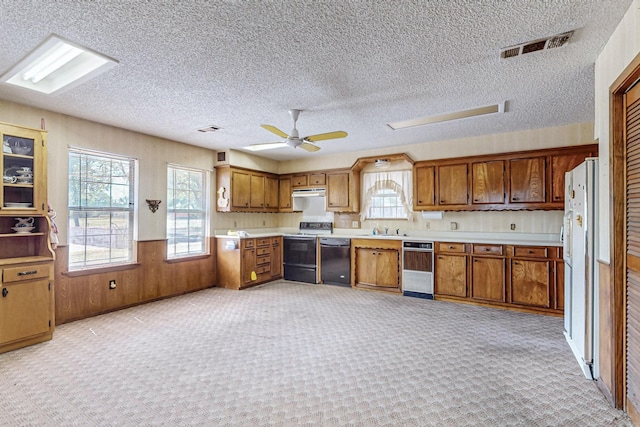 kitchen with brown cabinetry, black dishwasher, light countertops, and electric range oven