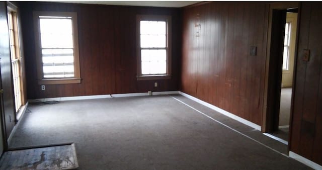 spare room with wood walls, plenty of natural light, and dark colored carpet