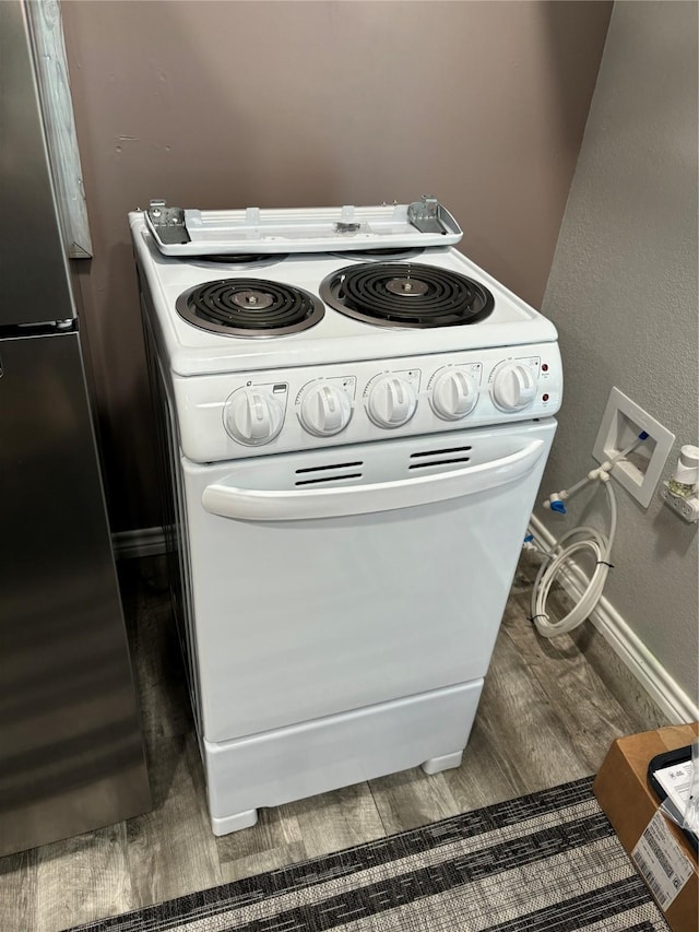 interior details featuring dark hardwood / wood-style flooring, stainless steel fridge, and white range with electric cooktop