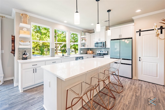 kitchen featuring white cabinets, a barn door, appliances with stainless steel finishes, a kitchen island, and a kitchen bar