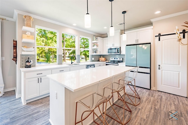 kitchen with a breakfast bar, appliances with stainless steel finishes, white cabinetry, a kitchen island, and a barn door