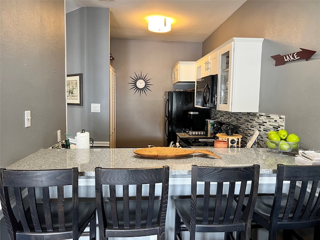 kitchen featuring a kitchen breakfast bar, black appliances, backsplash, kitchen peninsula, and light stone counters