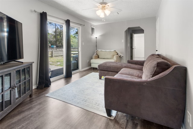 living room with a textured ceiling, ceiling fan, and dark hardwood / wood-style flooring