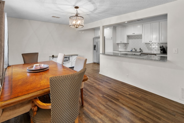 dining room with dark wood-type flooring, a textured ceiling, a chandelier, and sink