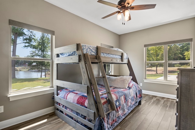 bedroom featuring ceiling fan, hardwood / wood-style flooring, a water view, and multiple windows