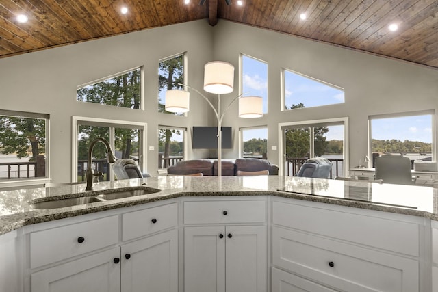 kitchen with light stone counters, wooden ceiling, a sink, white cabinetry, and open floor plan