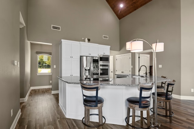 kitchen with dark hardwood / wood-style flooring, high vaulted ceiling, a center island with sink, and appliances with stainless steel finishes