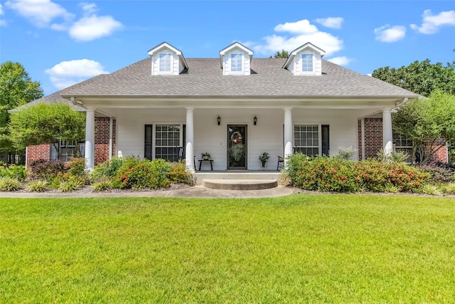 cape cod house with a porch, a front yard, roof with shingles, and brick siding